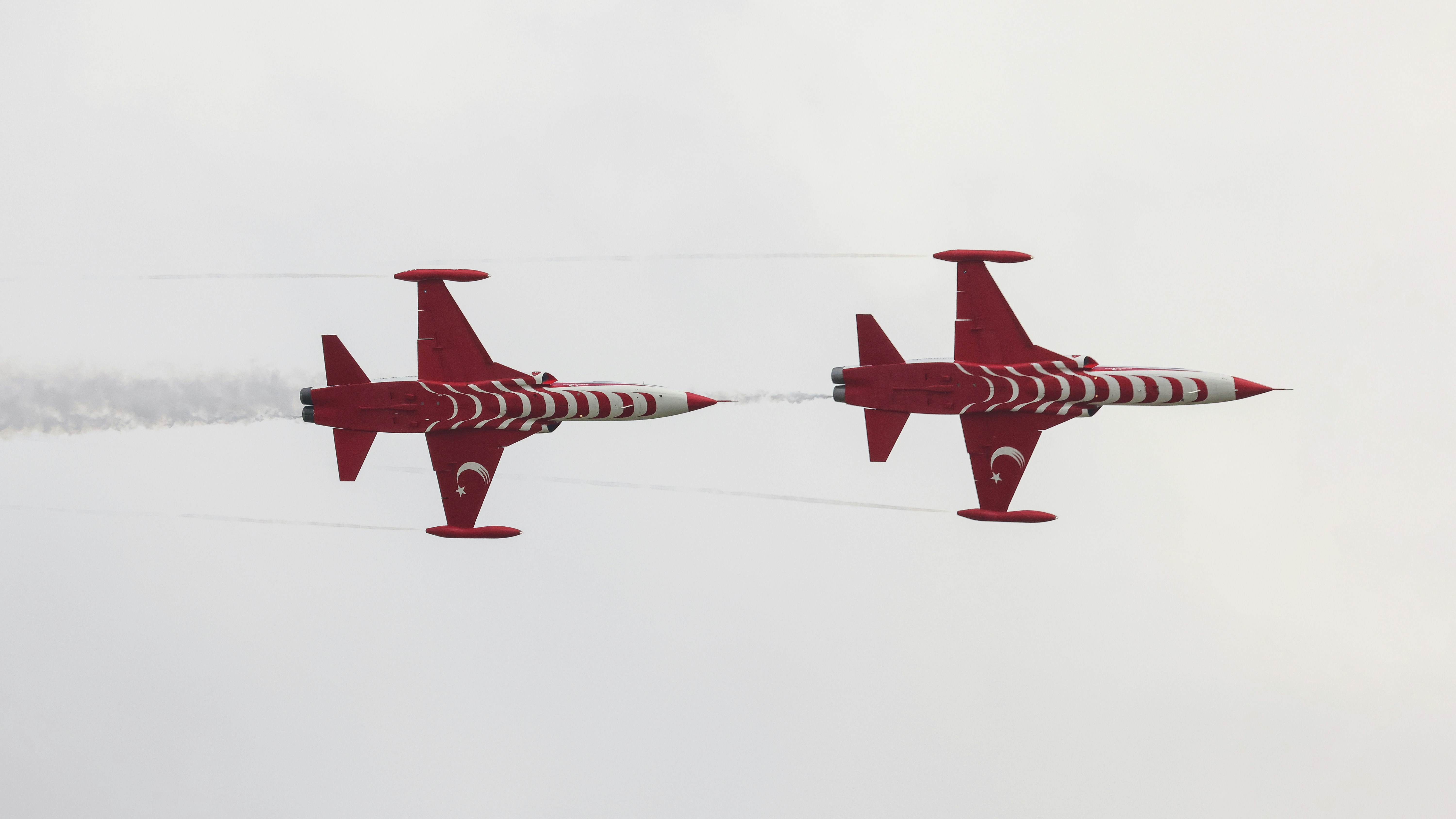 A couple of jets flying through a cloudy sky, A dynamic image of the Turkish Stars performing a mirror maneuver. The red and white jets, adorned with the Turkish flag, demonstrate incredible skill and synchronization.