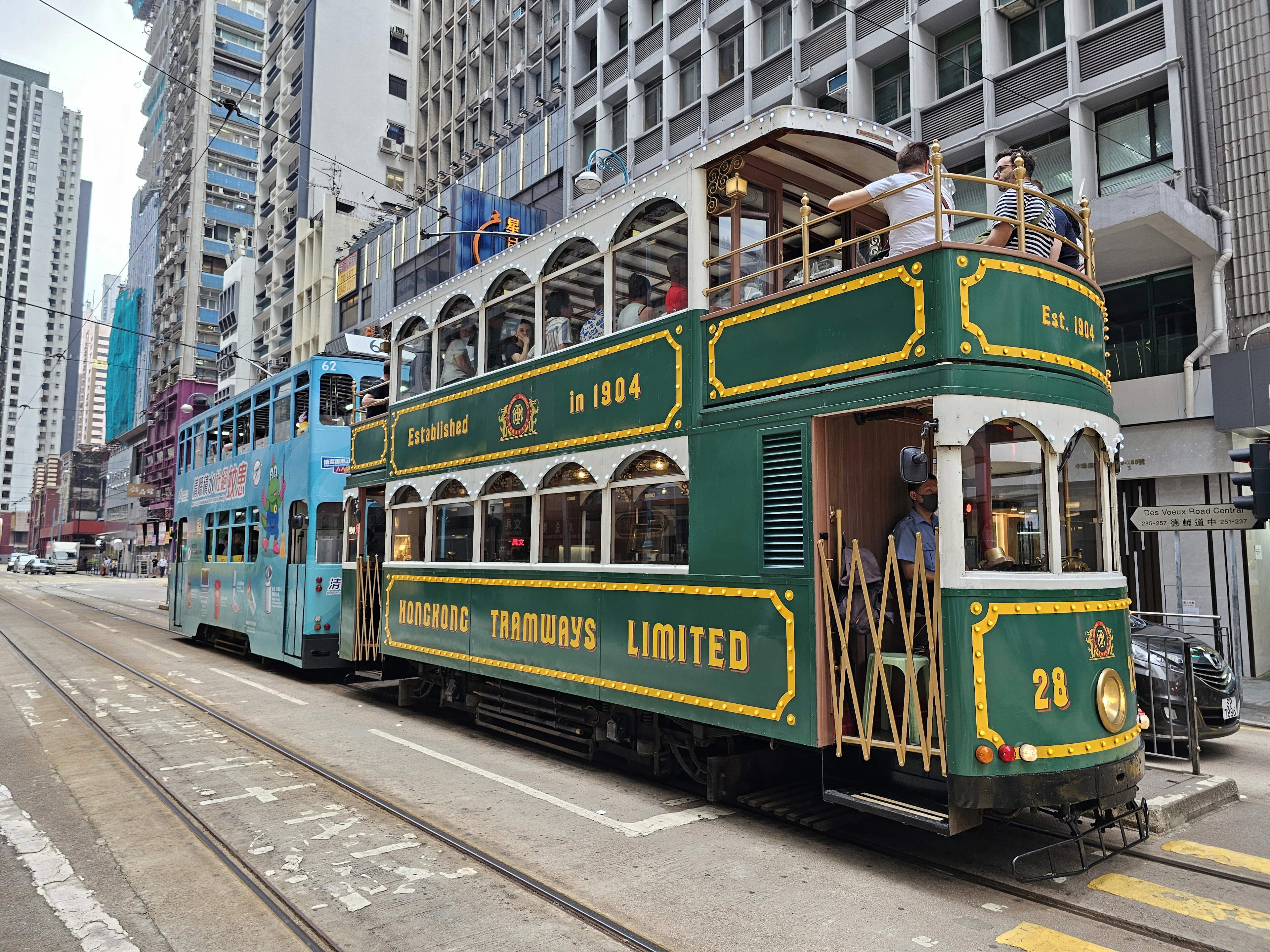 A heritage open-top ding ding tram lettered Hongkong Tramways Limited running between tower blocks on Hong Kong Island