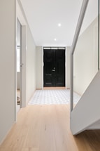 A white hallway with a black door and a wooden floor