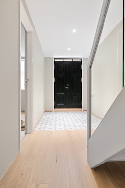 A white hallway with a black door and a wooden floor