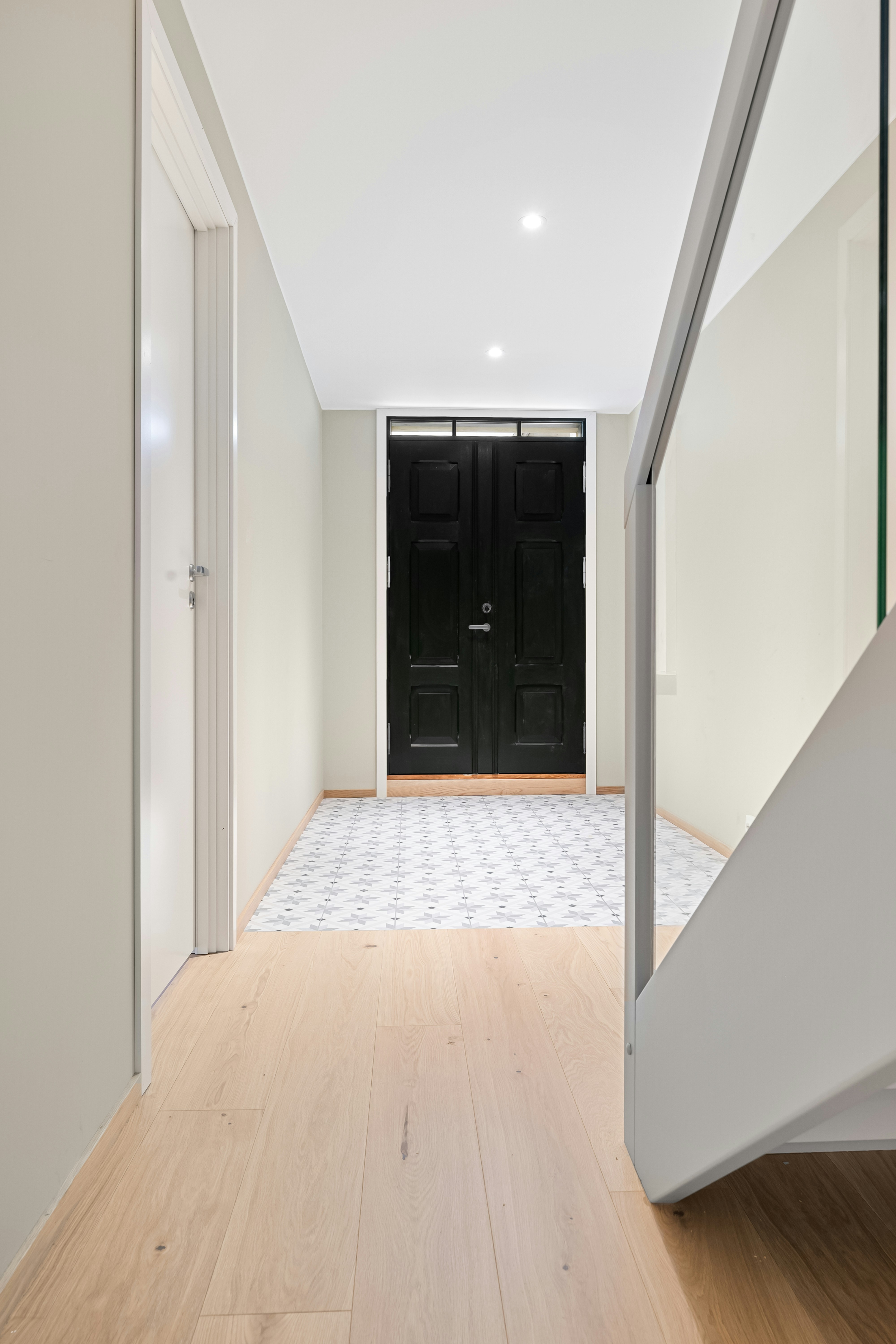 A white hallway with a black door and a wooden floor
