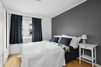 A bedroom with a bed, nightstand, and window