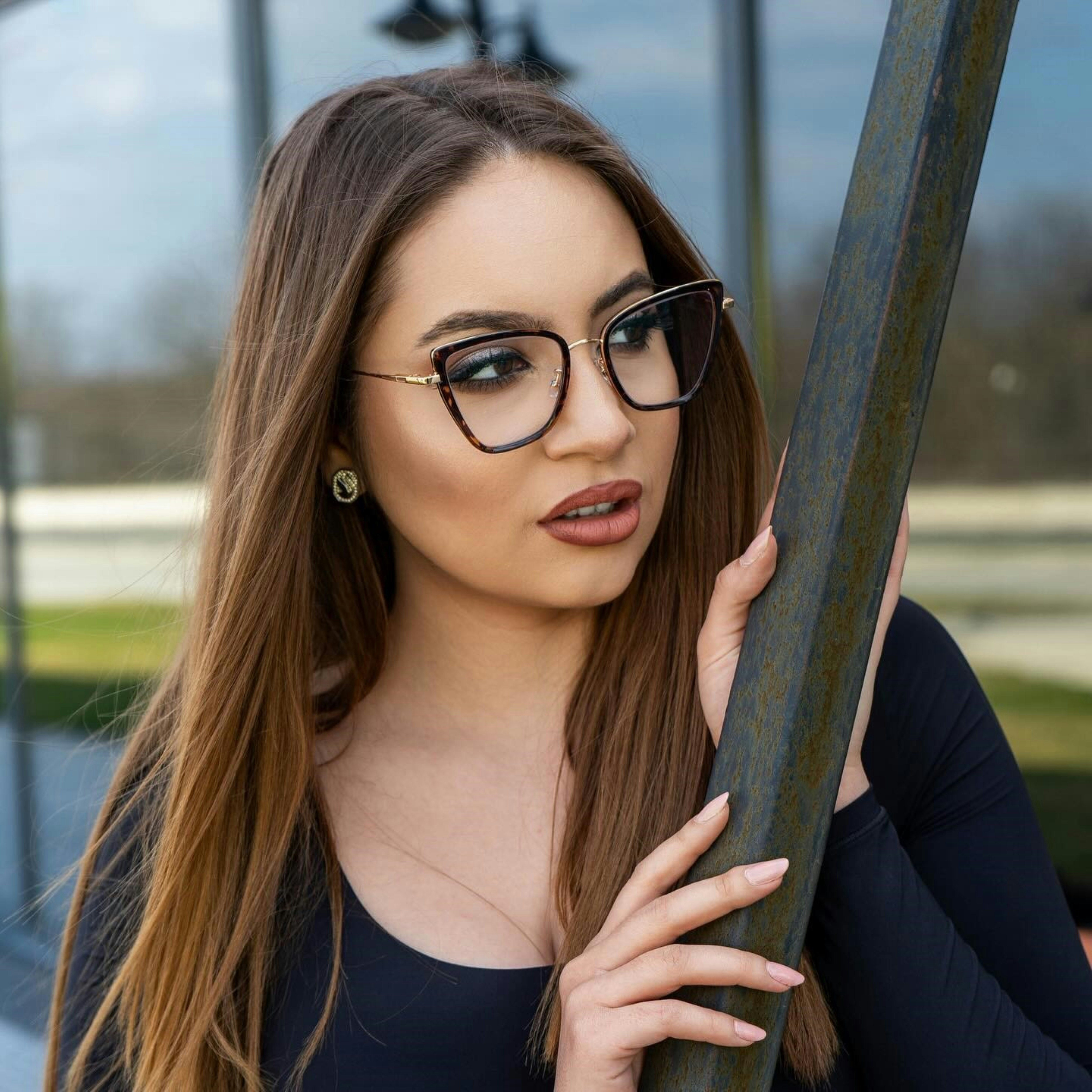 A woman wearing glasses leaning against a pole