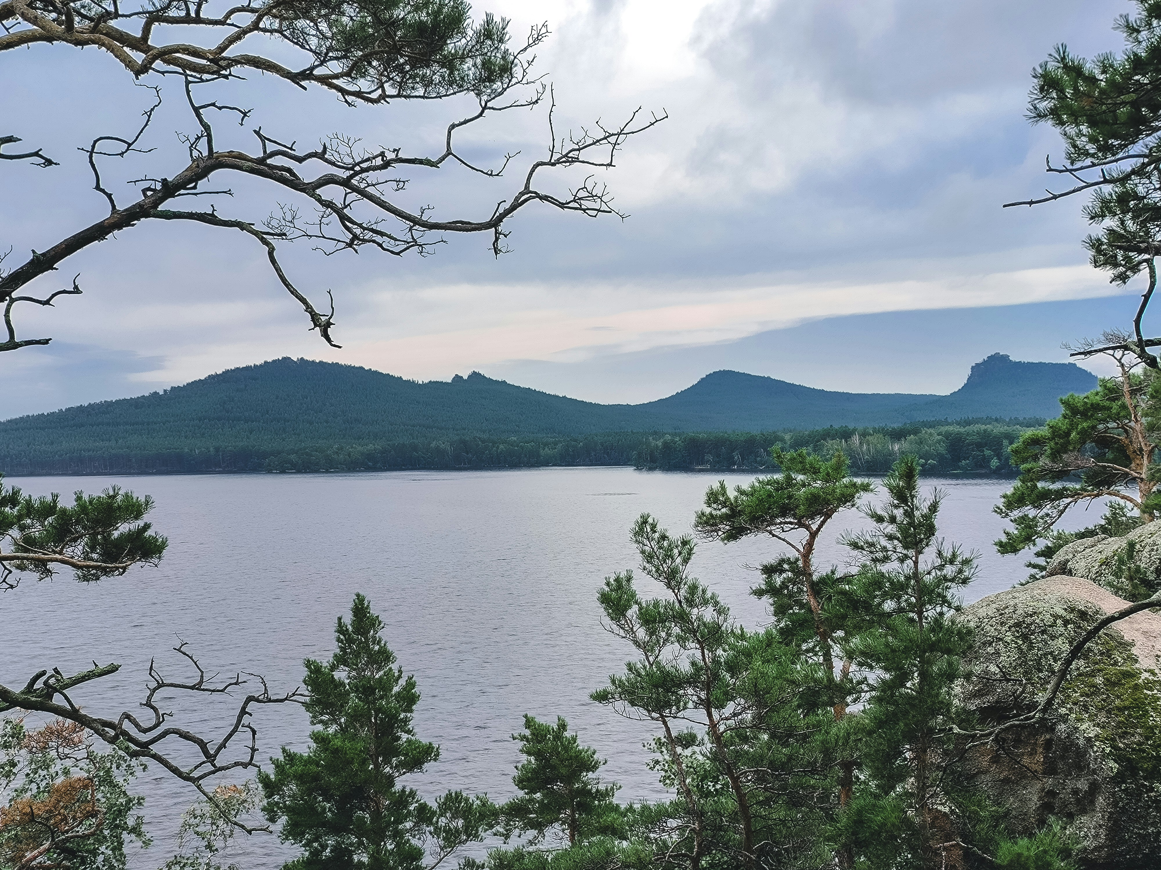 A lake surrounded by trees and mountains under a cloudy sky