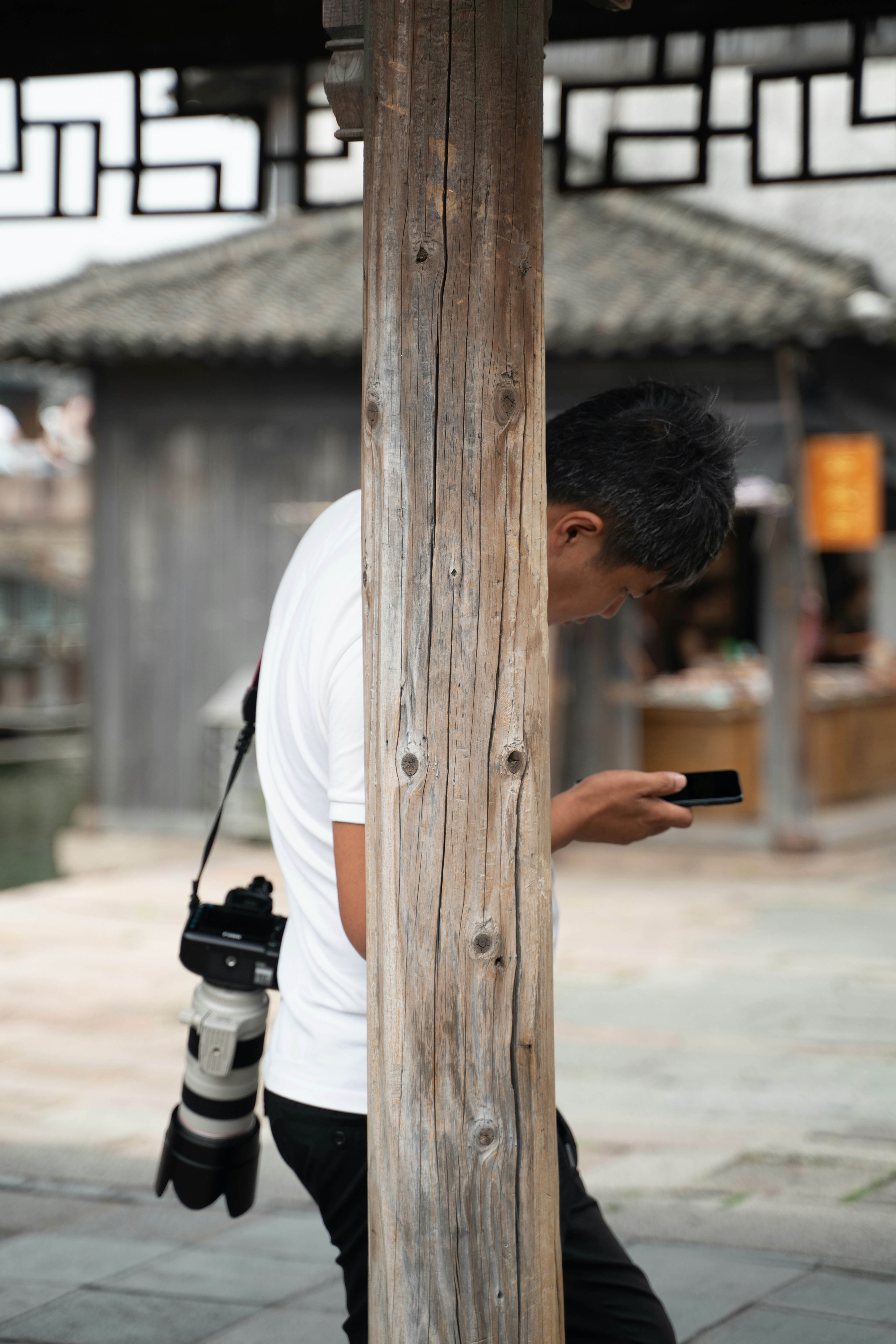 A man standing next to a wooden pole holding a camera