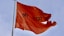 A red flag flying in the wind with a sky background