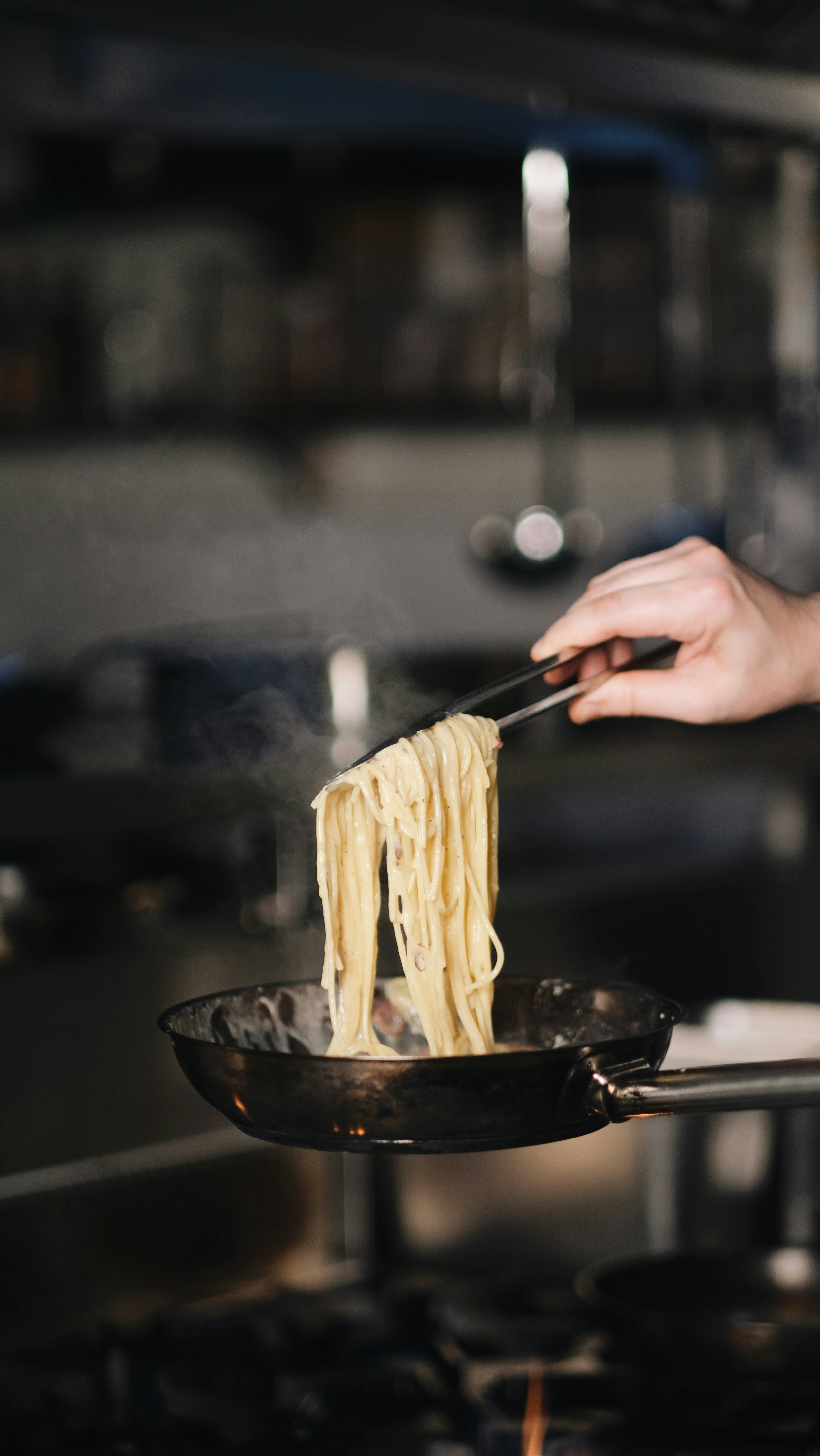 A person holding a frying pan with noodles in it