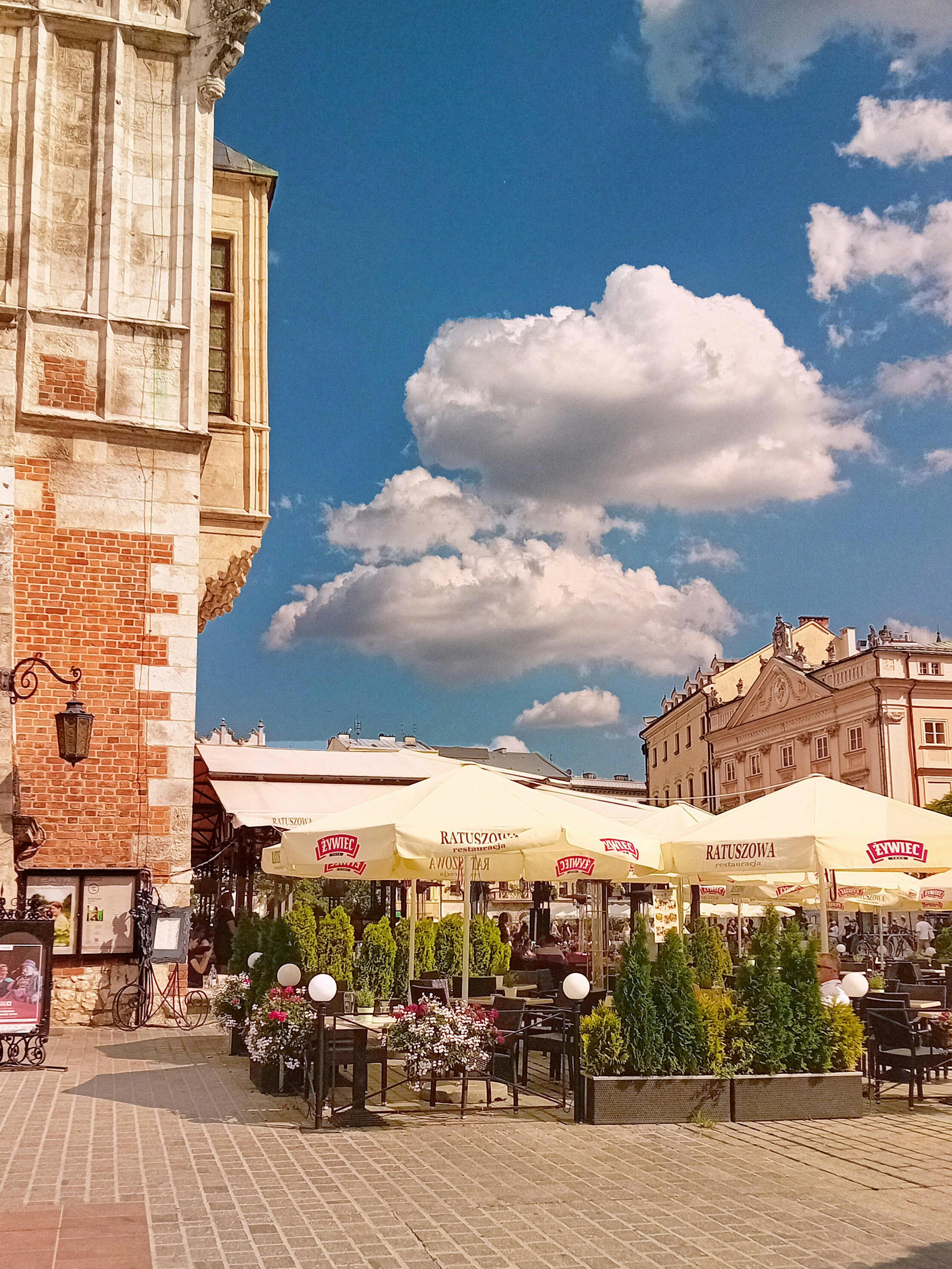 Terrasses et parasols sur la grand place de Cracovie sous un ciel nuageux