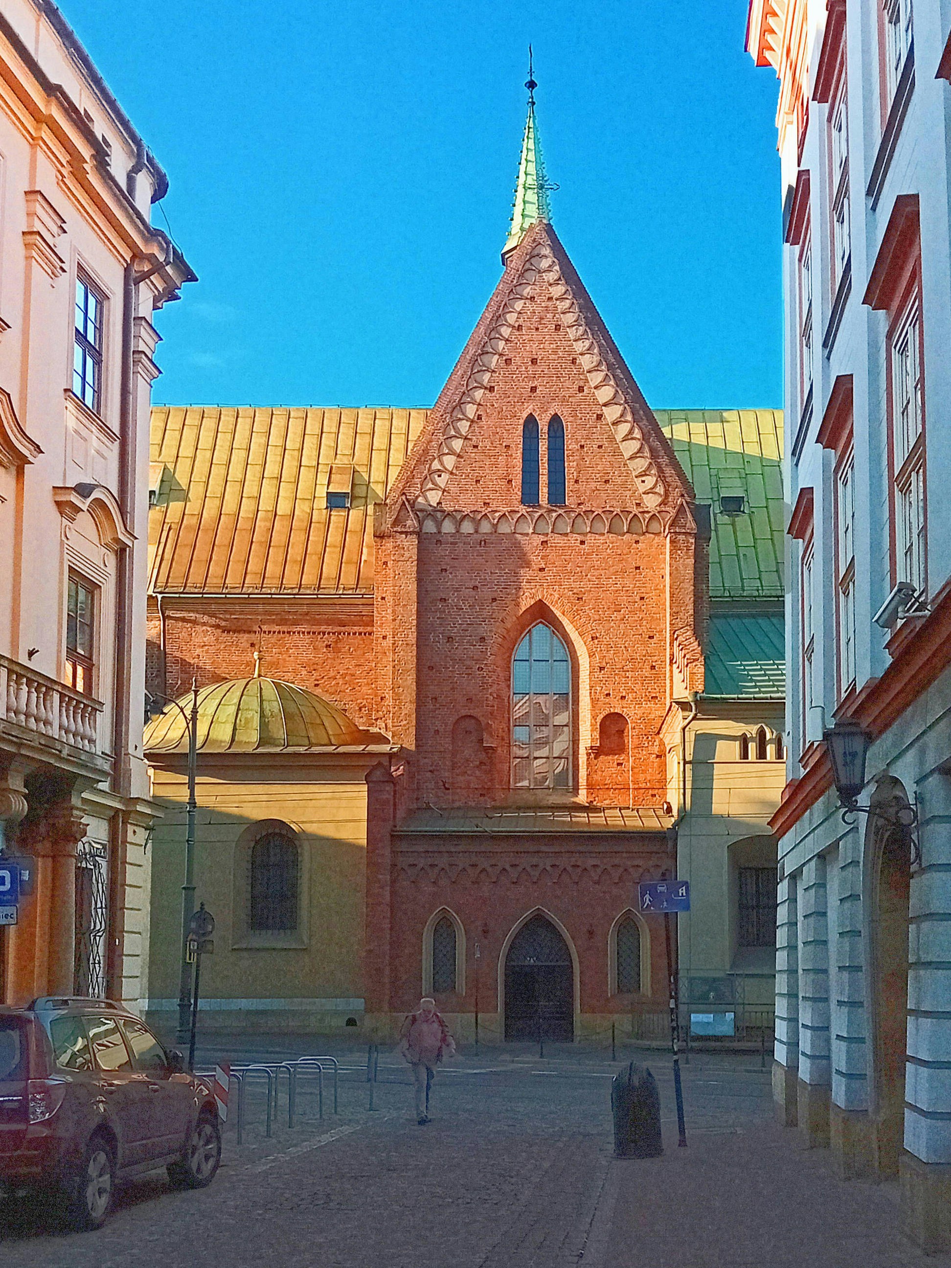 The other end of ul. Bracka in Old Town Krakow. North facade to Franciscan church in prominent shadows of morning sun. Orange brick, yellow copper roof and blue skies