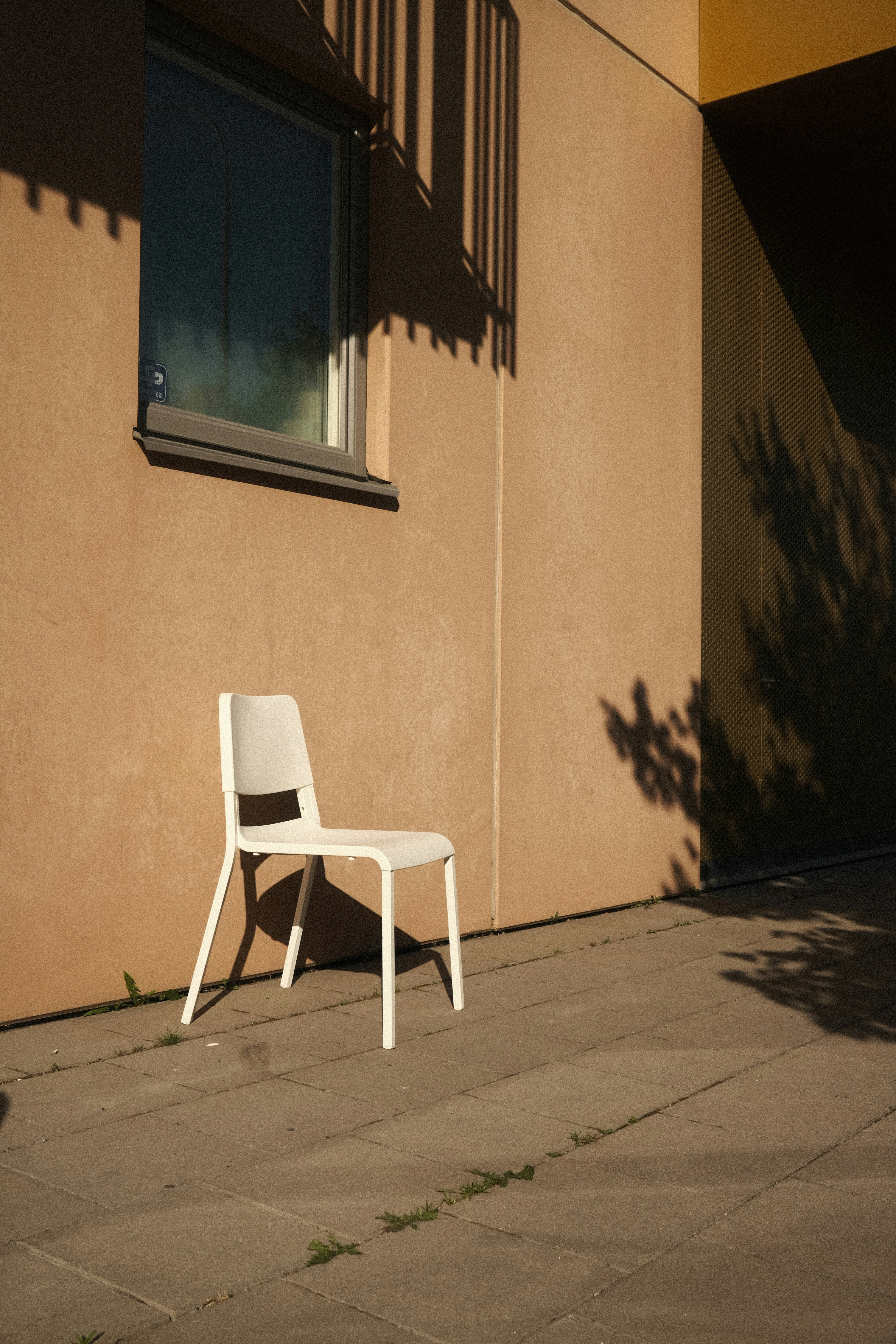 Ein weißer Stuhl sitzt auf einem Bürgersteig neben einem Gebäude