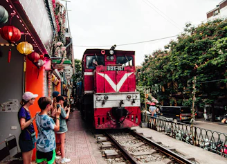 A red train traveling down train tracks next to a crowd of people