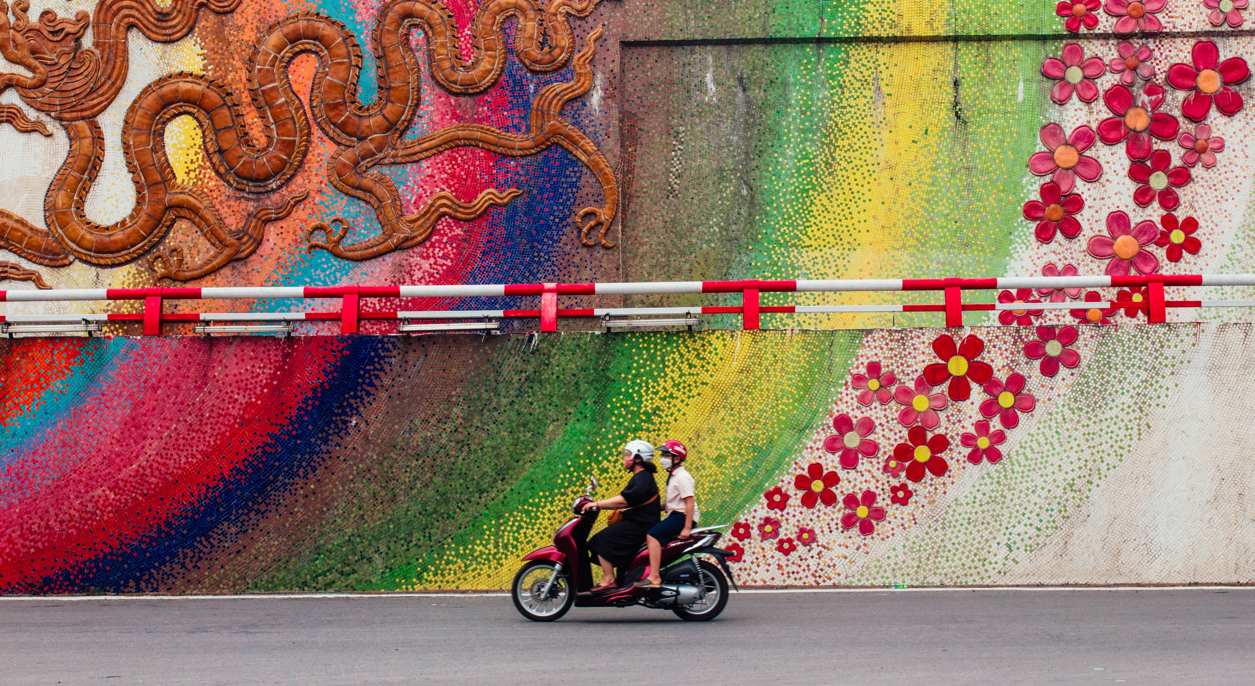 A man riding a motorcycle down a street next to a colorful wall