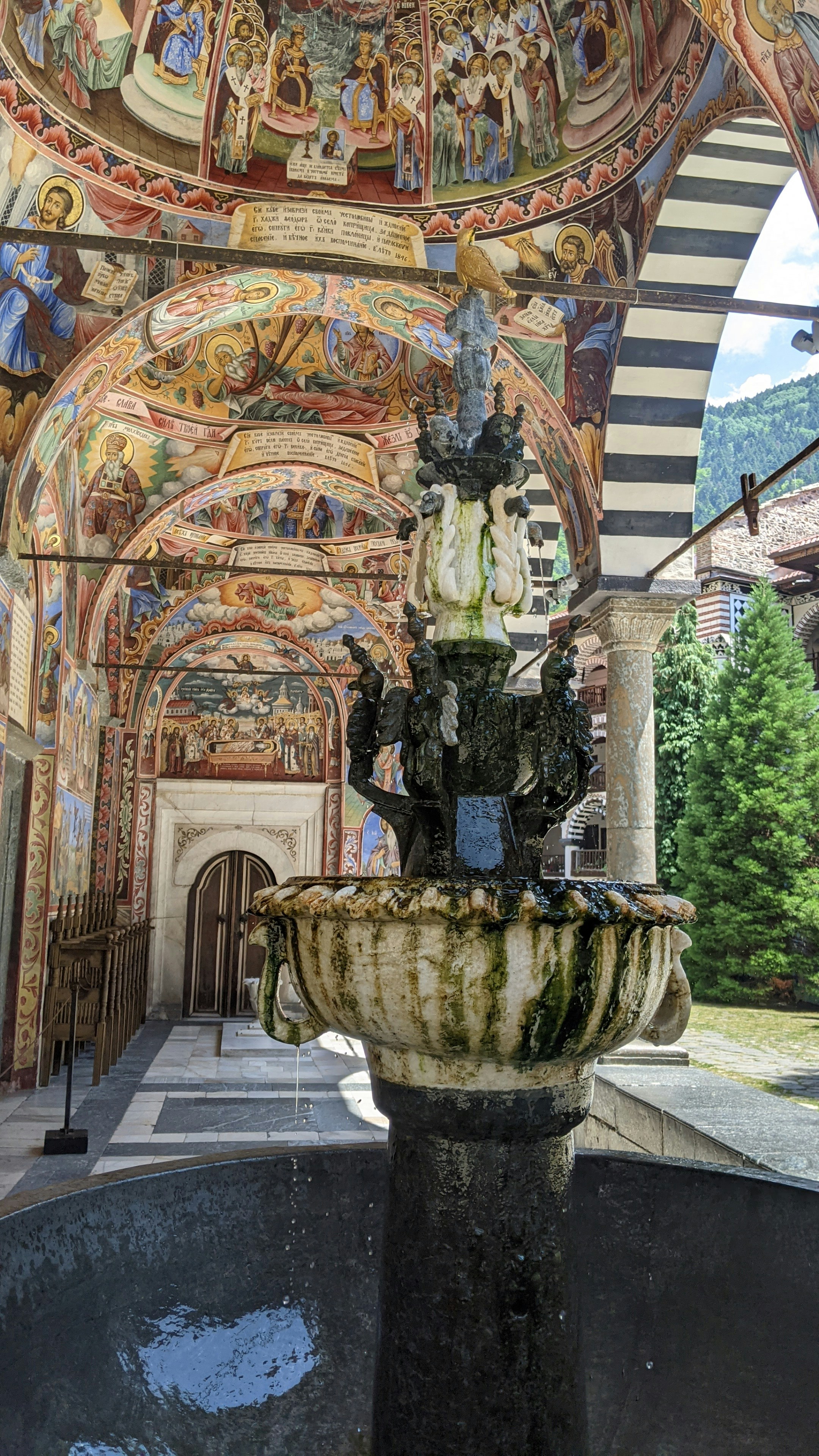 A fountain inside of a building with paintings on the walls