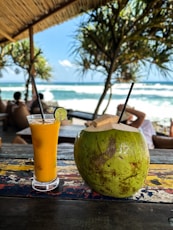 A glass of orange juice next to a coconut on a table