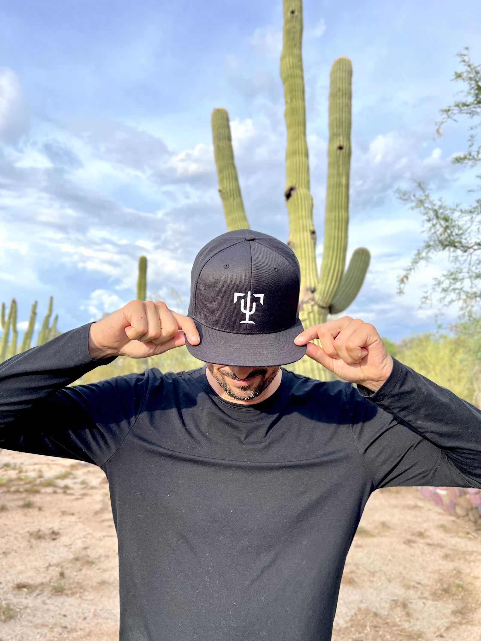 A man wearing a hat standing in front of a cactus