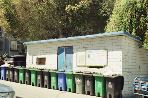 A row of green and blue trash cans next to a building