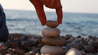 A person stacking rocks on a beach with the ocean in the background