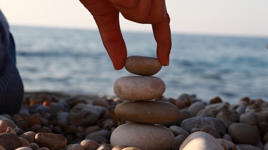A person stacking rocks on a beach with the ocean in the background
