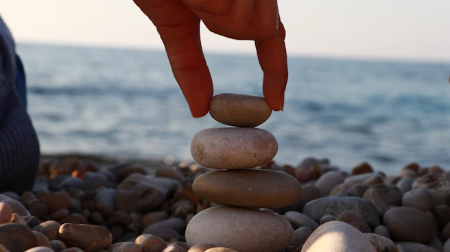 A person stacking rocks on a beach with the ocean in the background