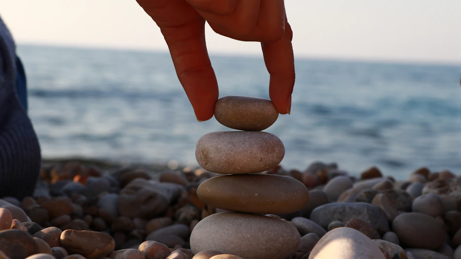 A person stacking rocks on a beach with the ocean in the background