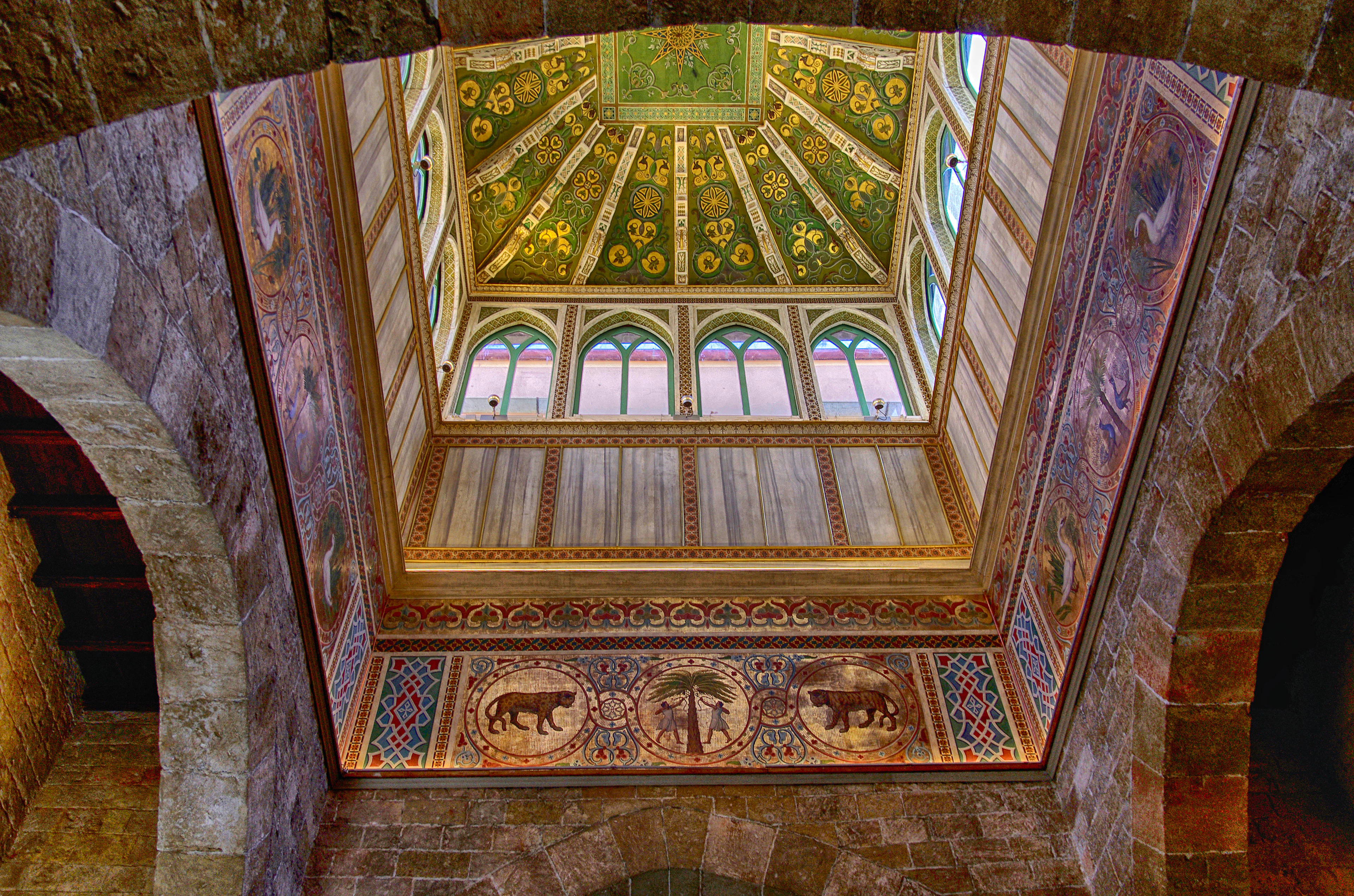 A gilded, frescoed vaulted ceiling with painted medallions and arched windows inside a historic Palermo palace hall.