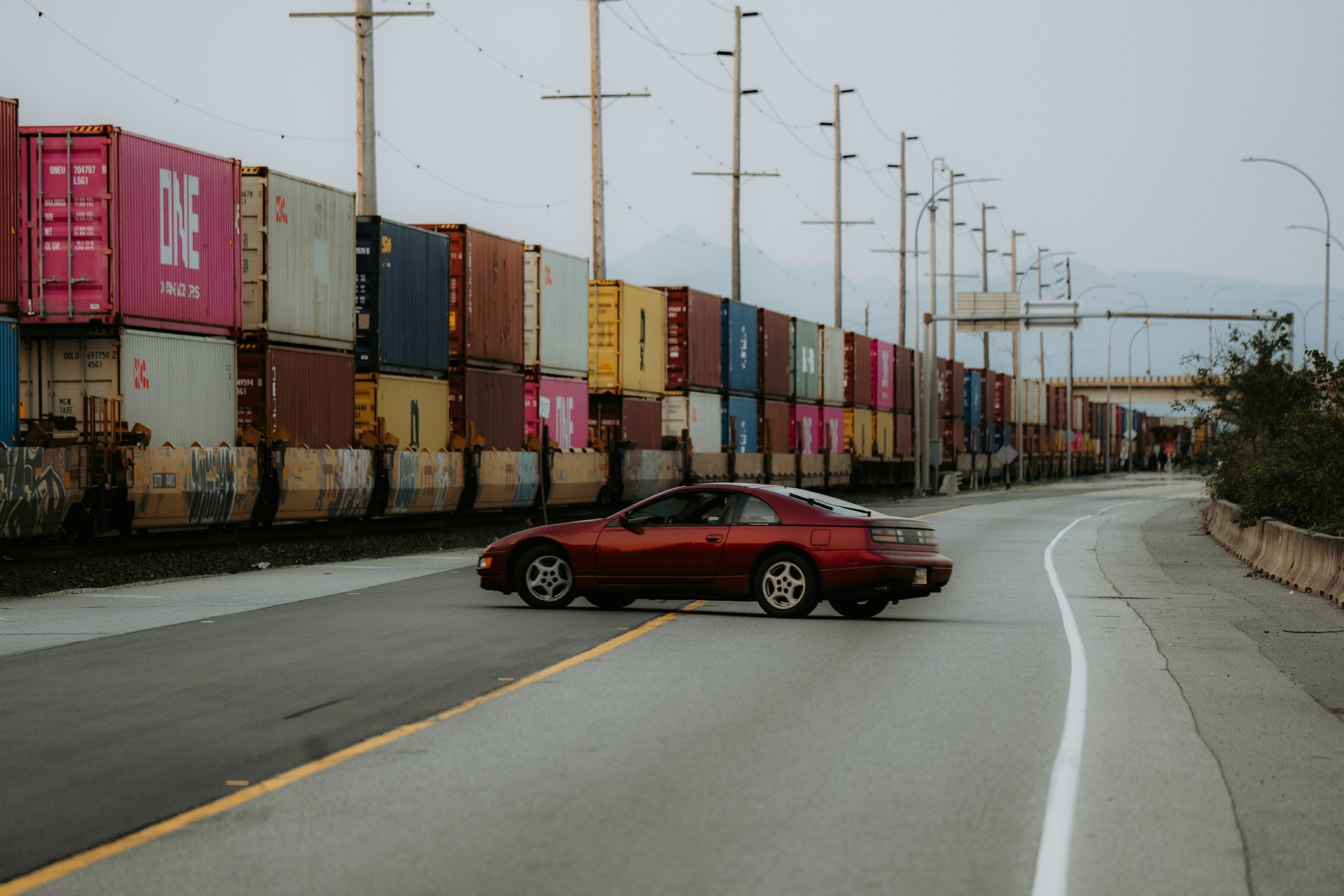 A red car driving down a street next to a train