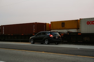 A black car driving down a road next to a train