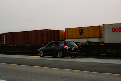 A black car driving down a road next to a train