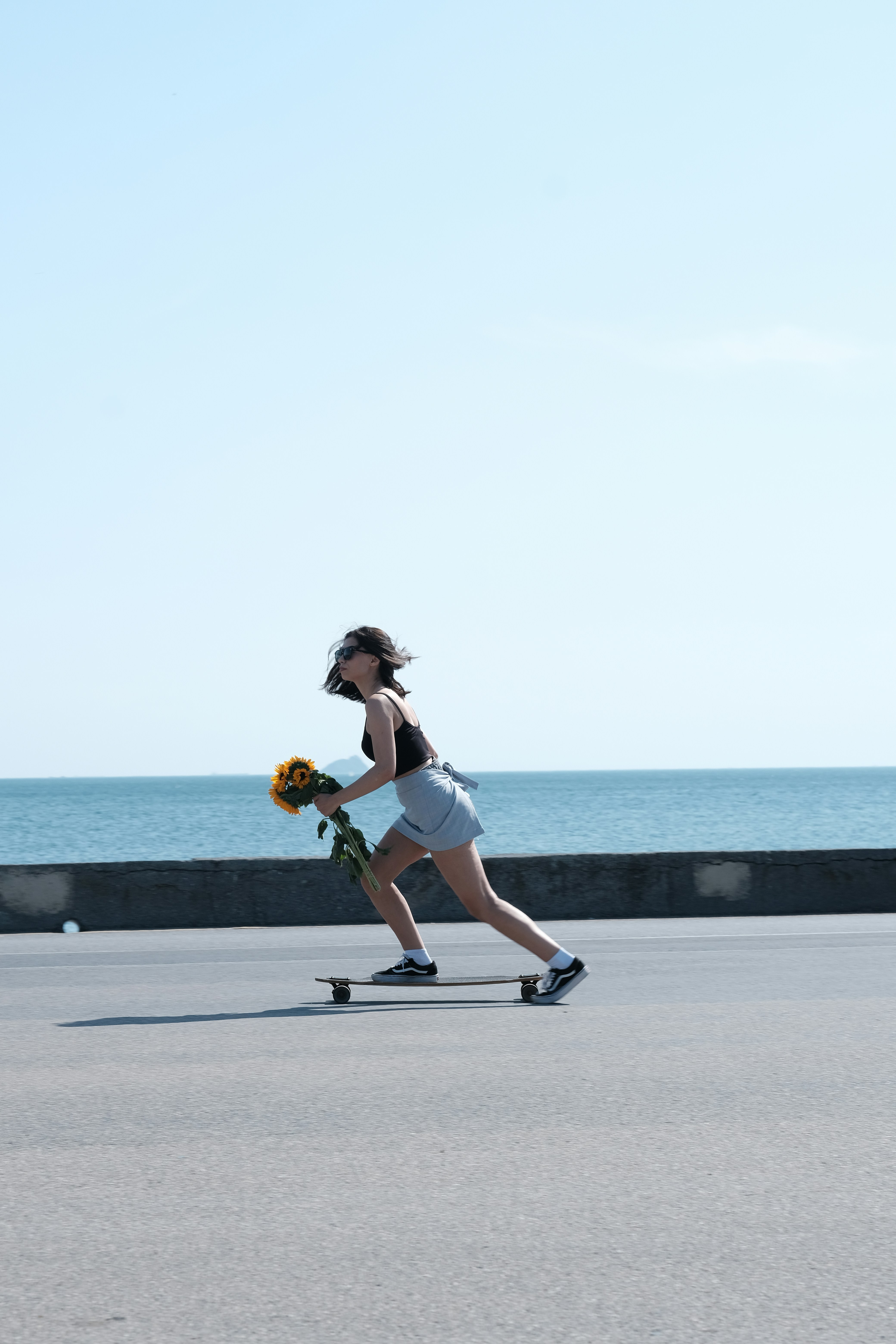 A woman riding a skateboard down a street next to the ocean