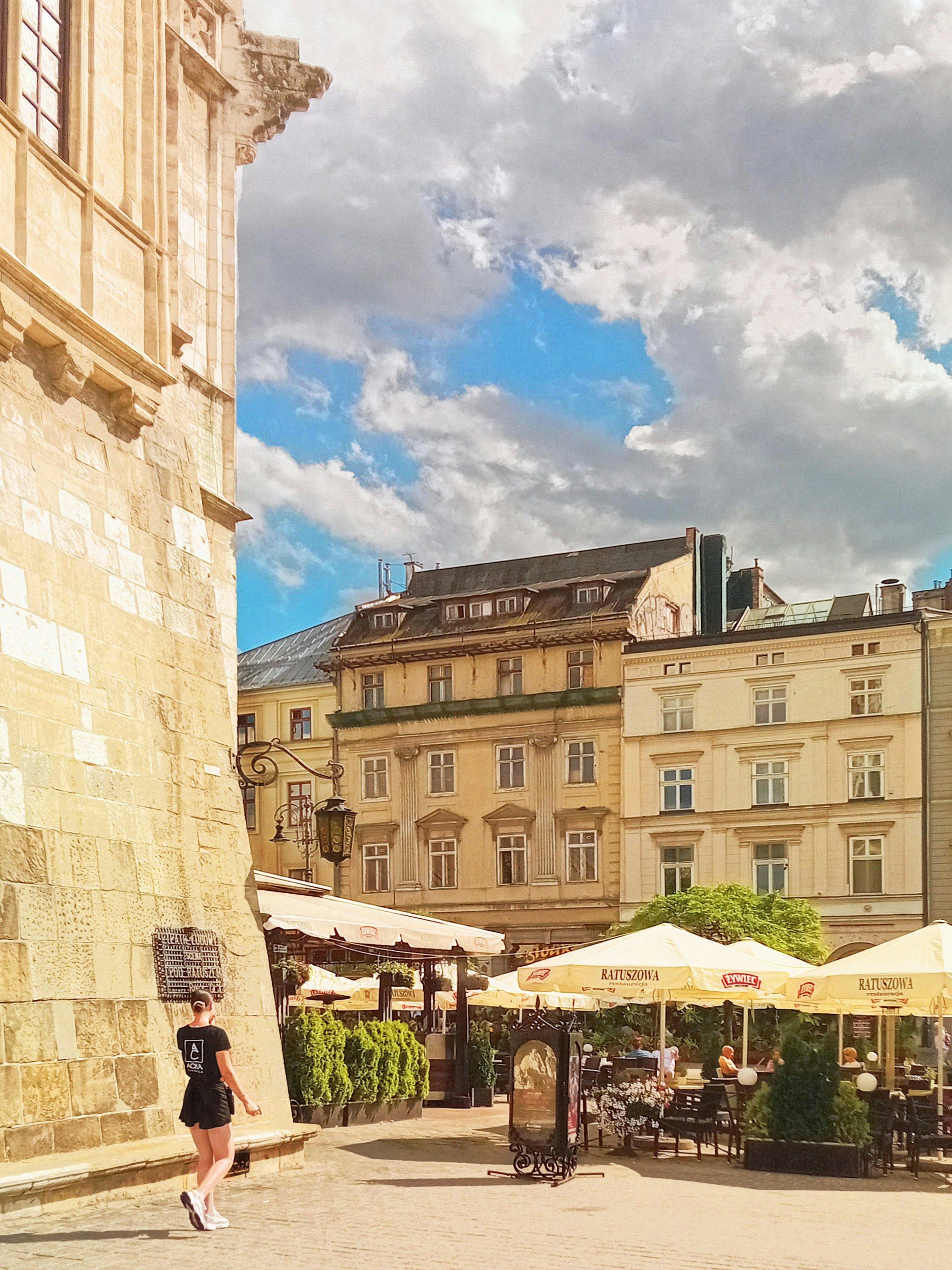 Femme marchant seule sur la place du marché de Cracovie bordée de bâtiments historiques