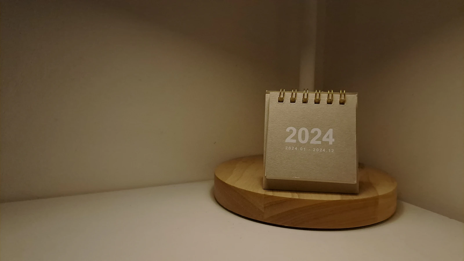 Offener Tischkalender neben einer Lampe auf hellem Holzschreibtisch mit ruhigem Licht