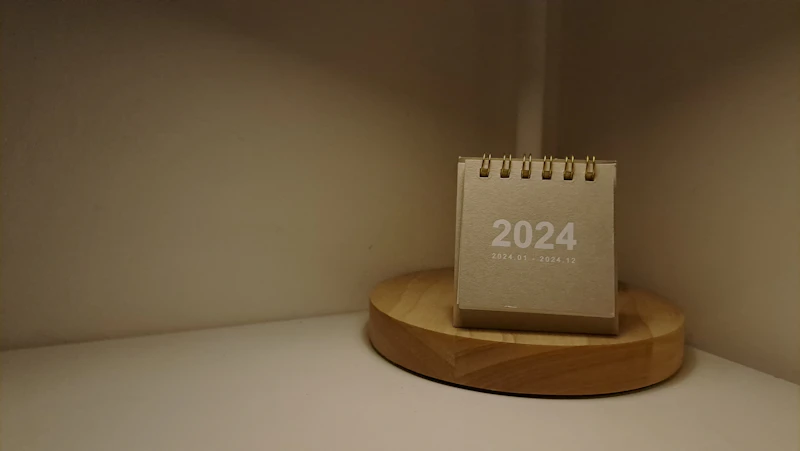Offener Tischkalender neben einer Lampe auf hellem Holzschreibtisch mit ruhigem Licht