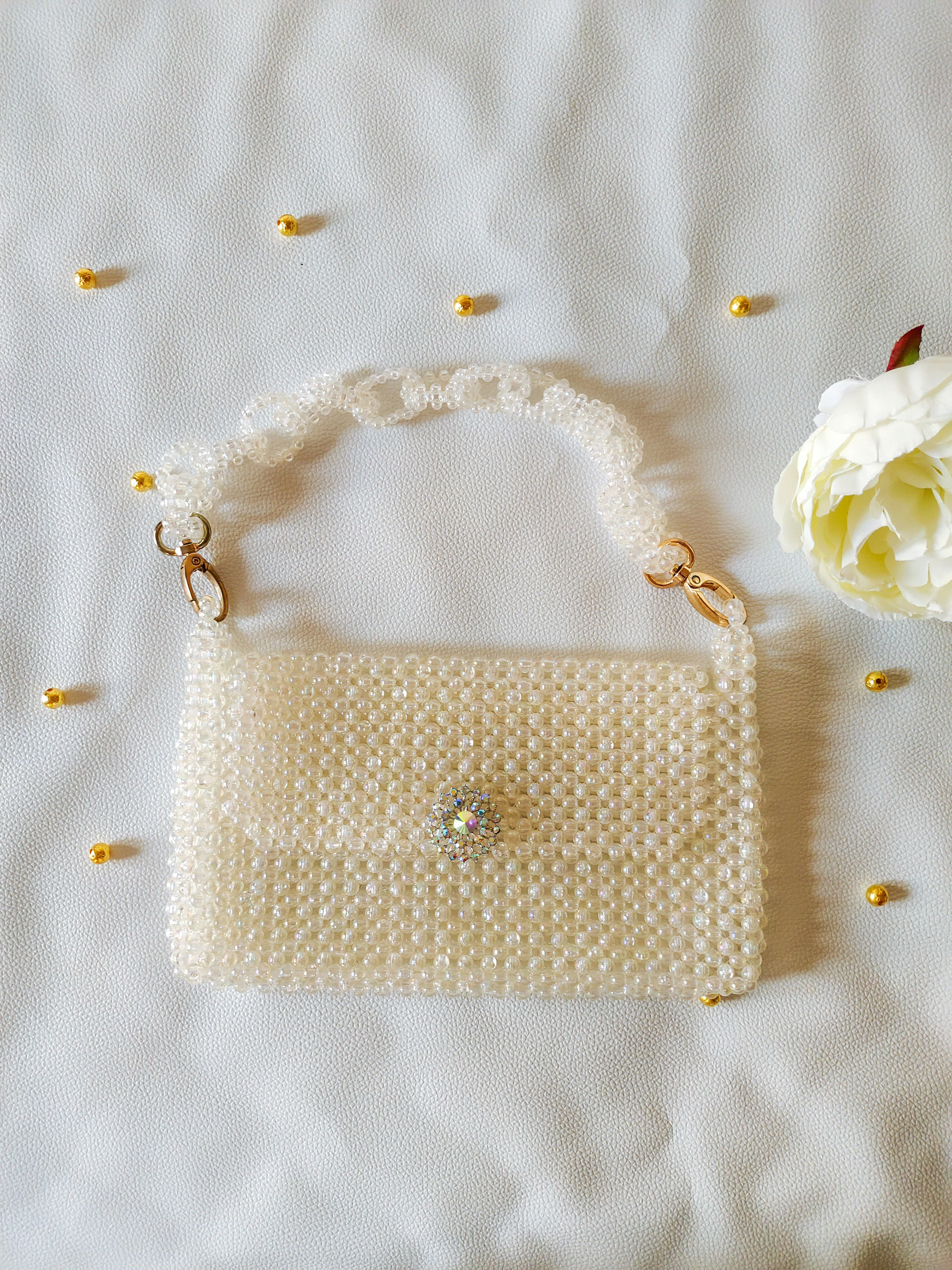 A white purse sitting on top of a bed next to a flower