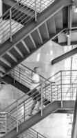 A black and white photo of a man walking down a stair case
