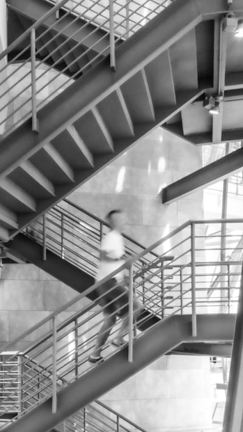 A black and white photo of a man walking down a stair case