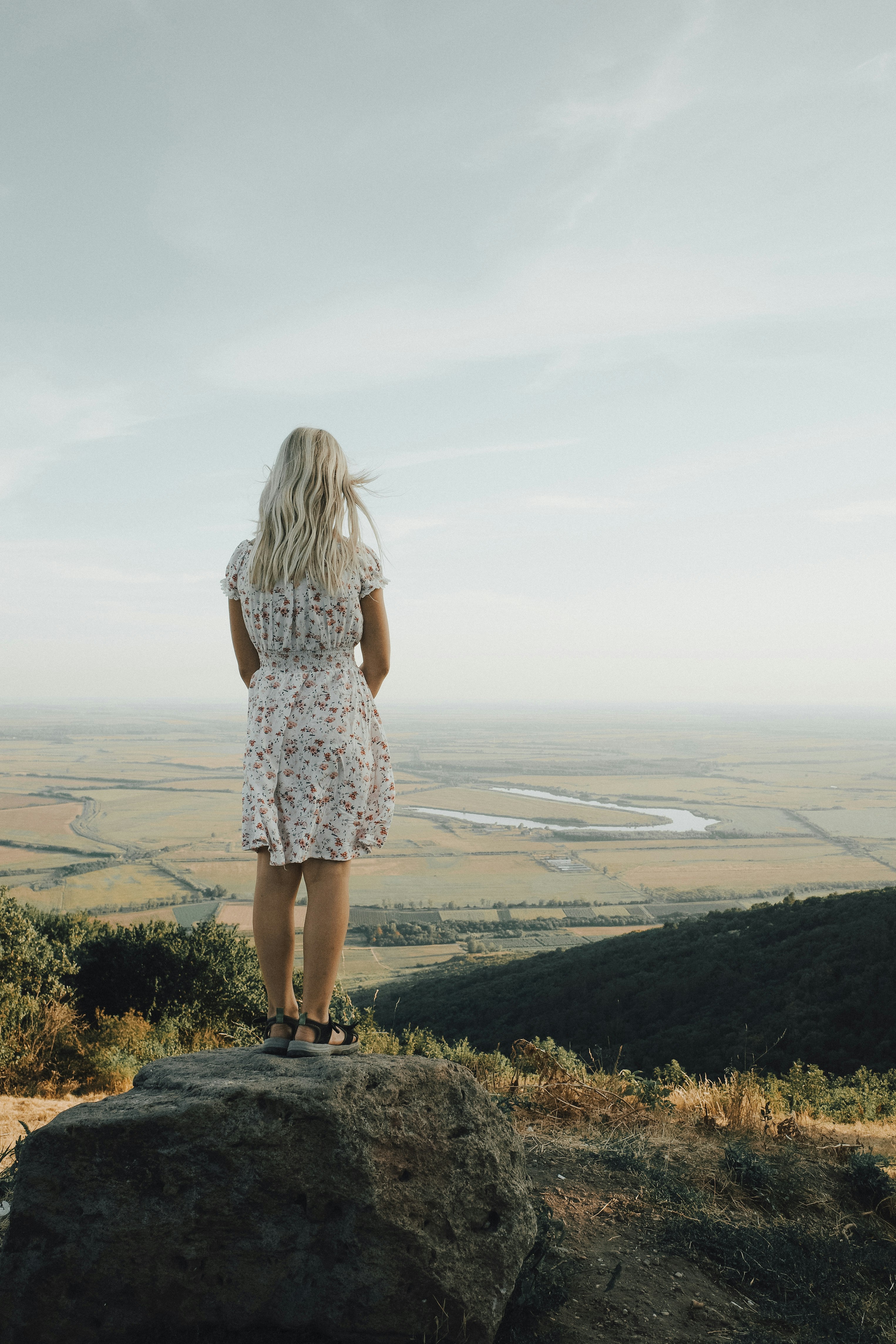 A woman standing on top of a rock looking out over a valley