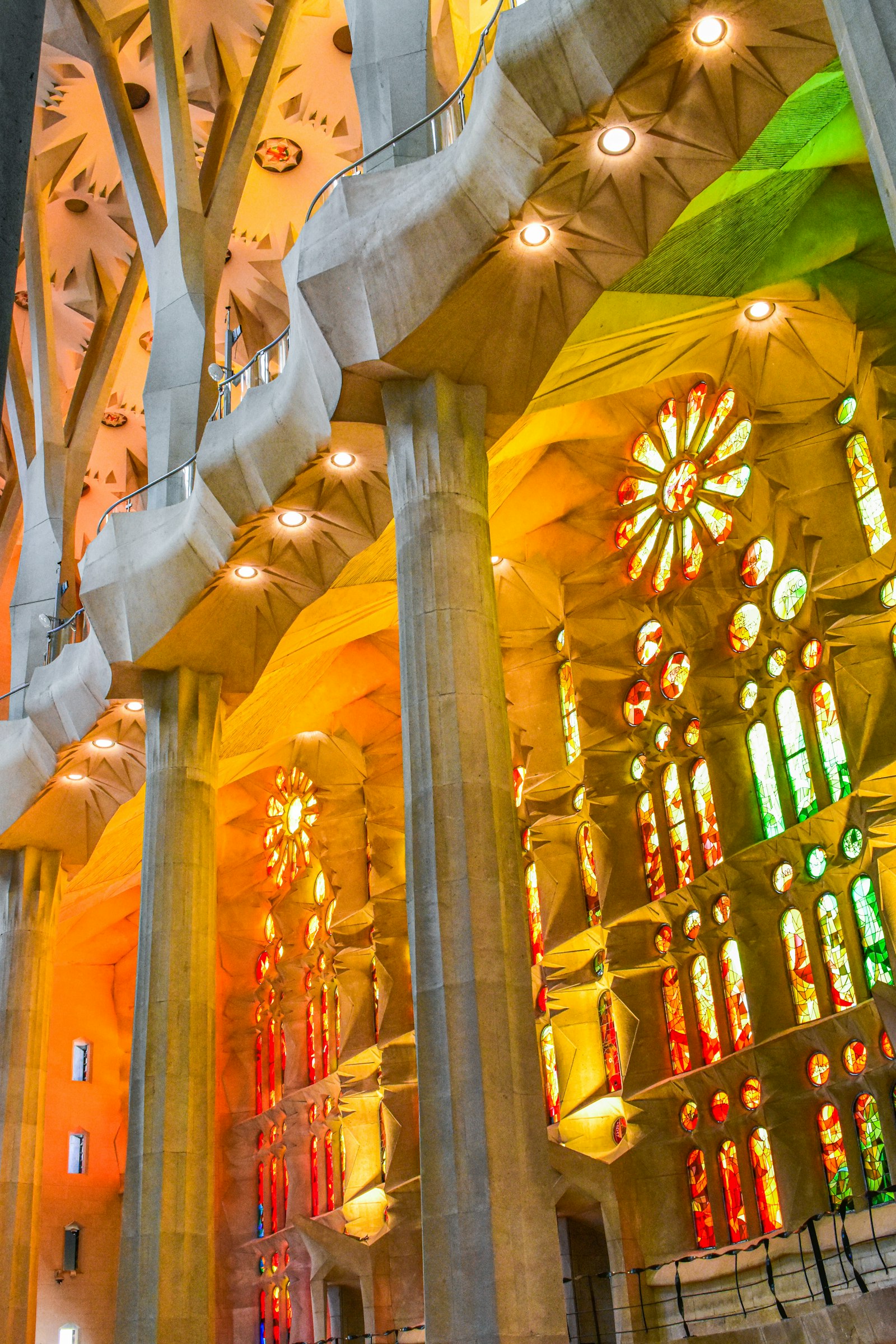 Tree-like stone columns inside the Sagrada Família branching toward the ceiling, lit orange and green by walls of stained glass