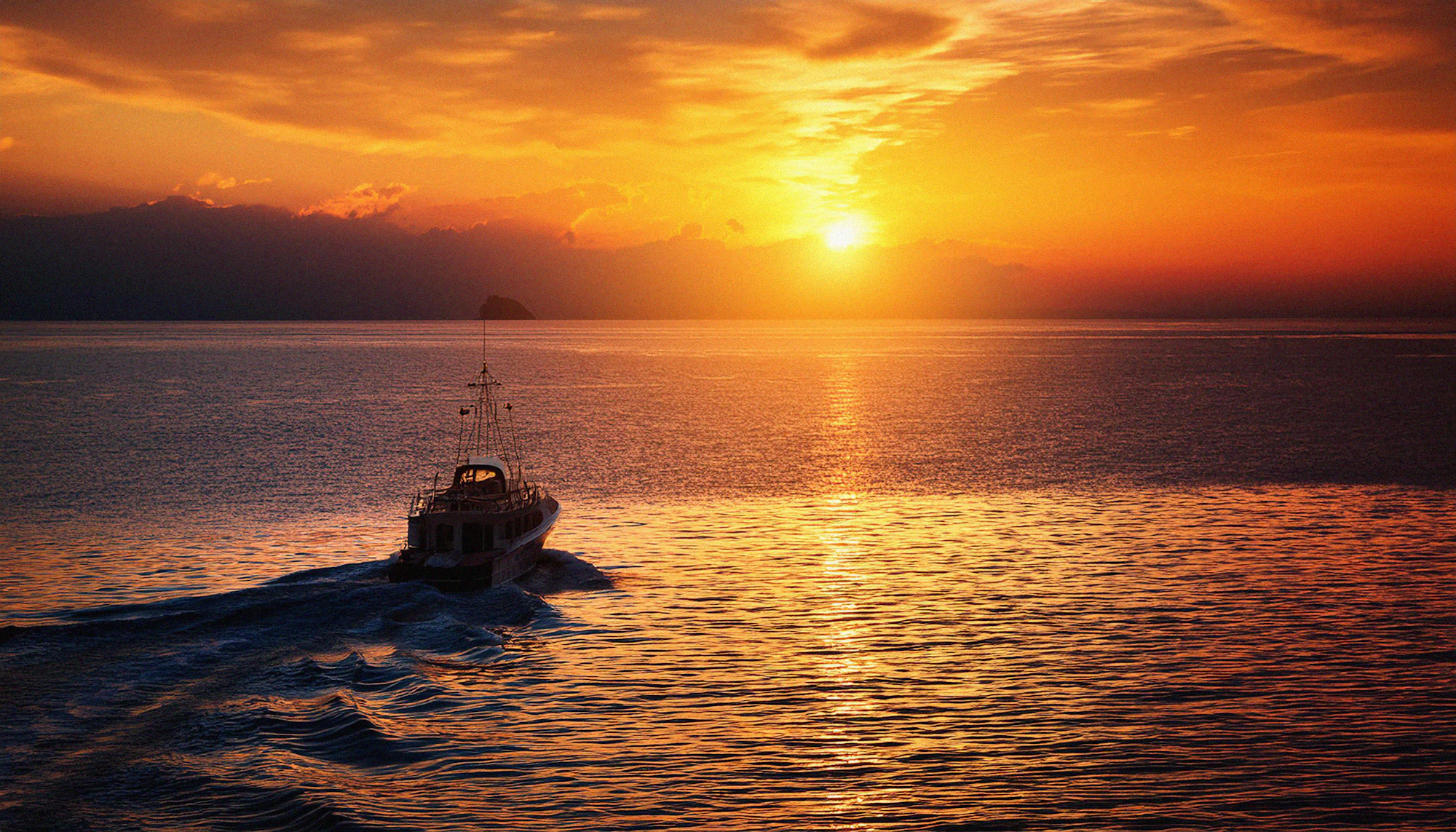A boat crossing open water beneath a golden sunset