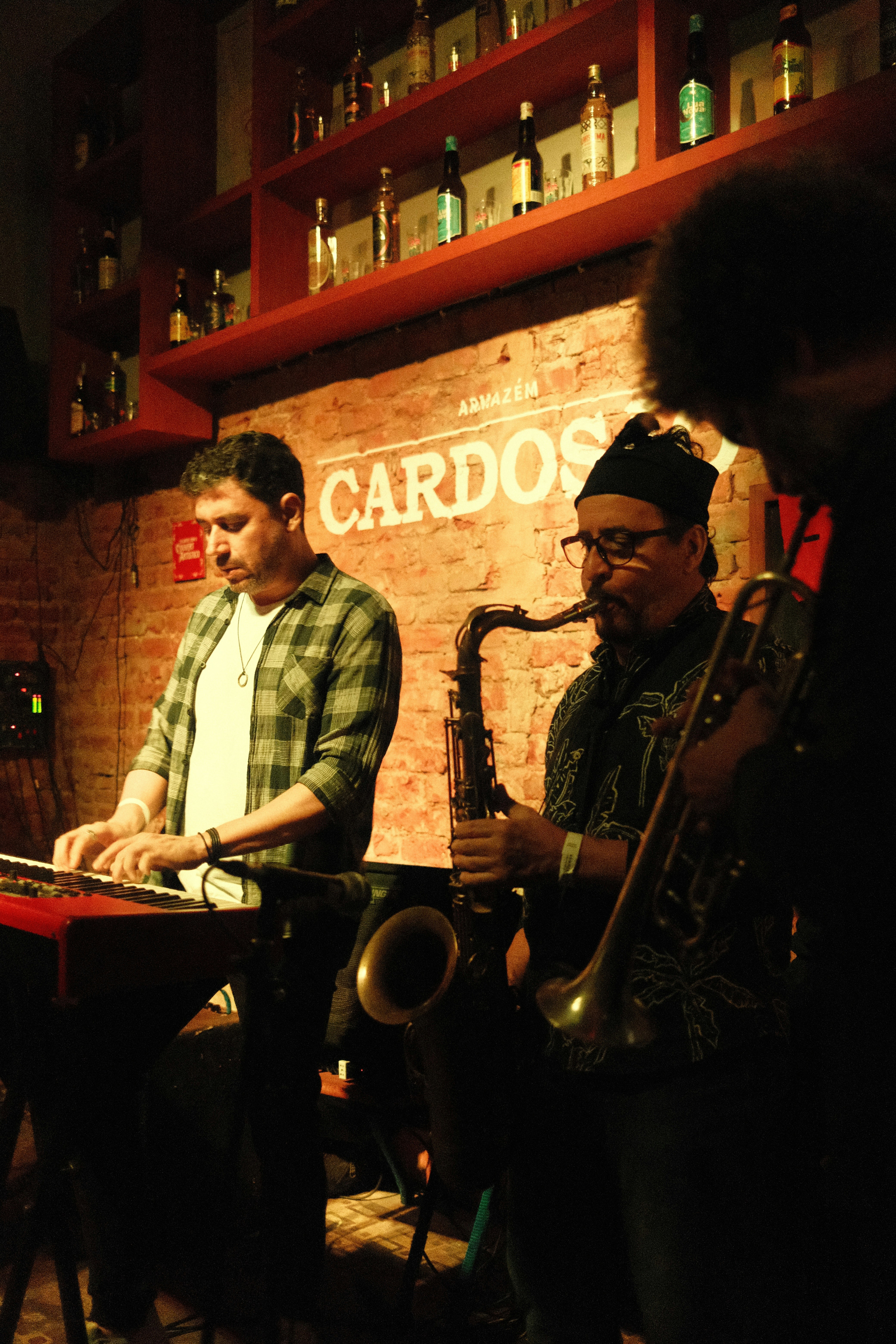 Three musicians play keyboard, saxophone, and trumpet at a bar.