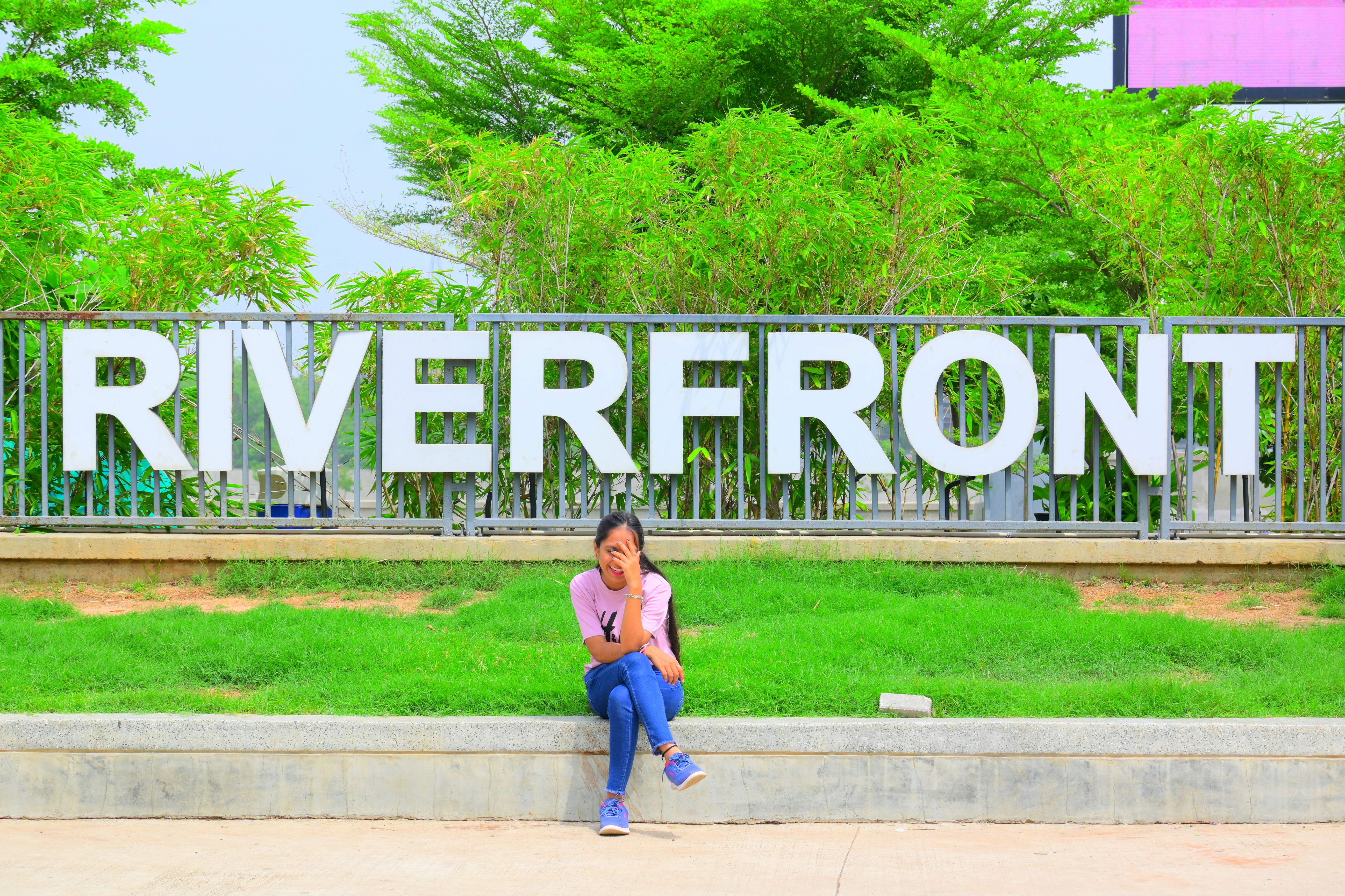A woman sitting on a bench in front of a riverfront sign