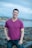A man in a purple shirt standing on a rocky beach