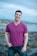 A man in a purple shirt standing on a rocky beach