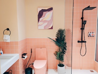 A bathroom with pink tiles and a plant in the corner