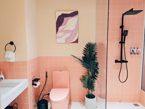 A bathroom with pink tiles and a plant in the corner