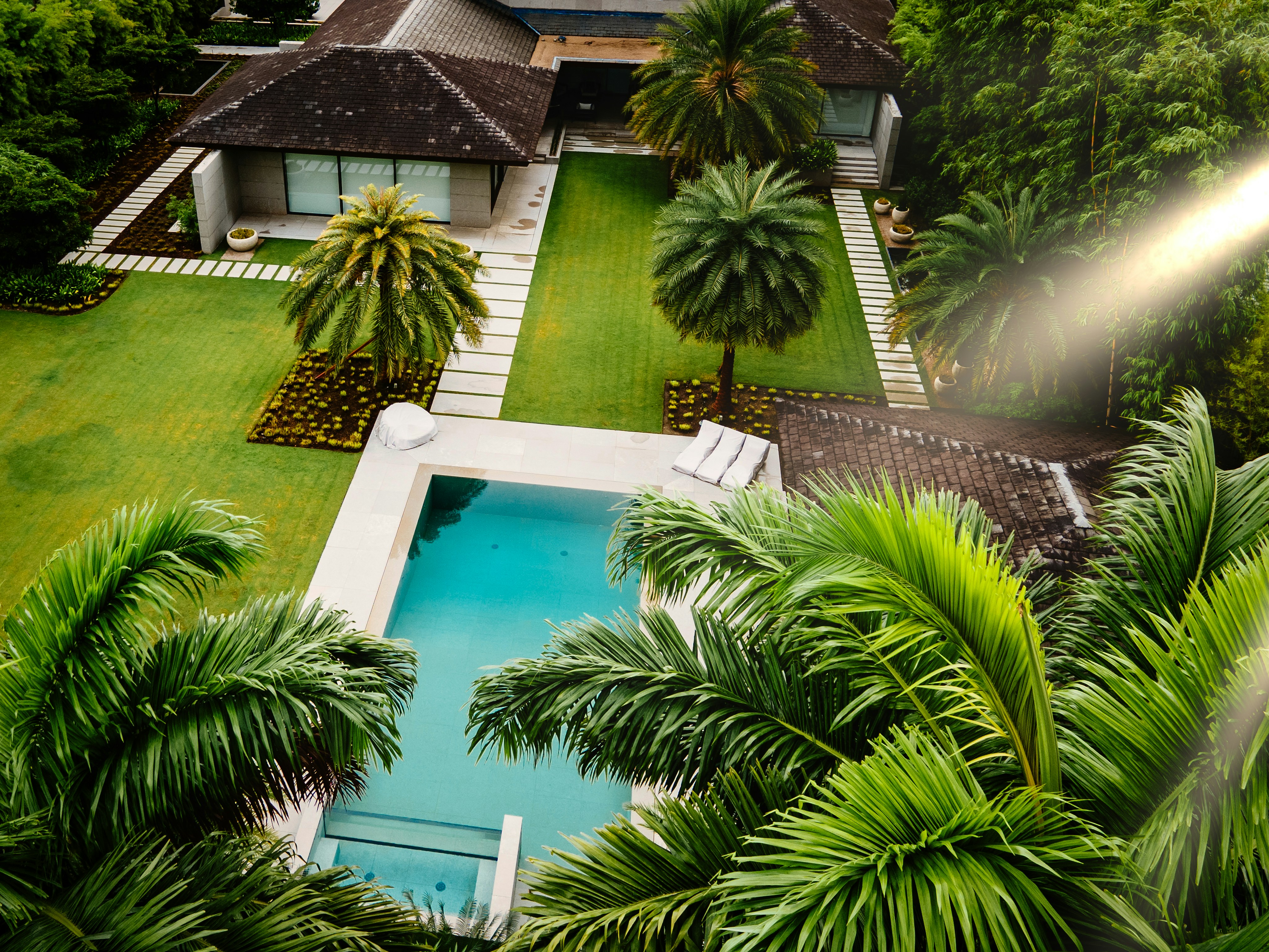 An aerial view of a house with a pool surrounded by palm trees