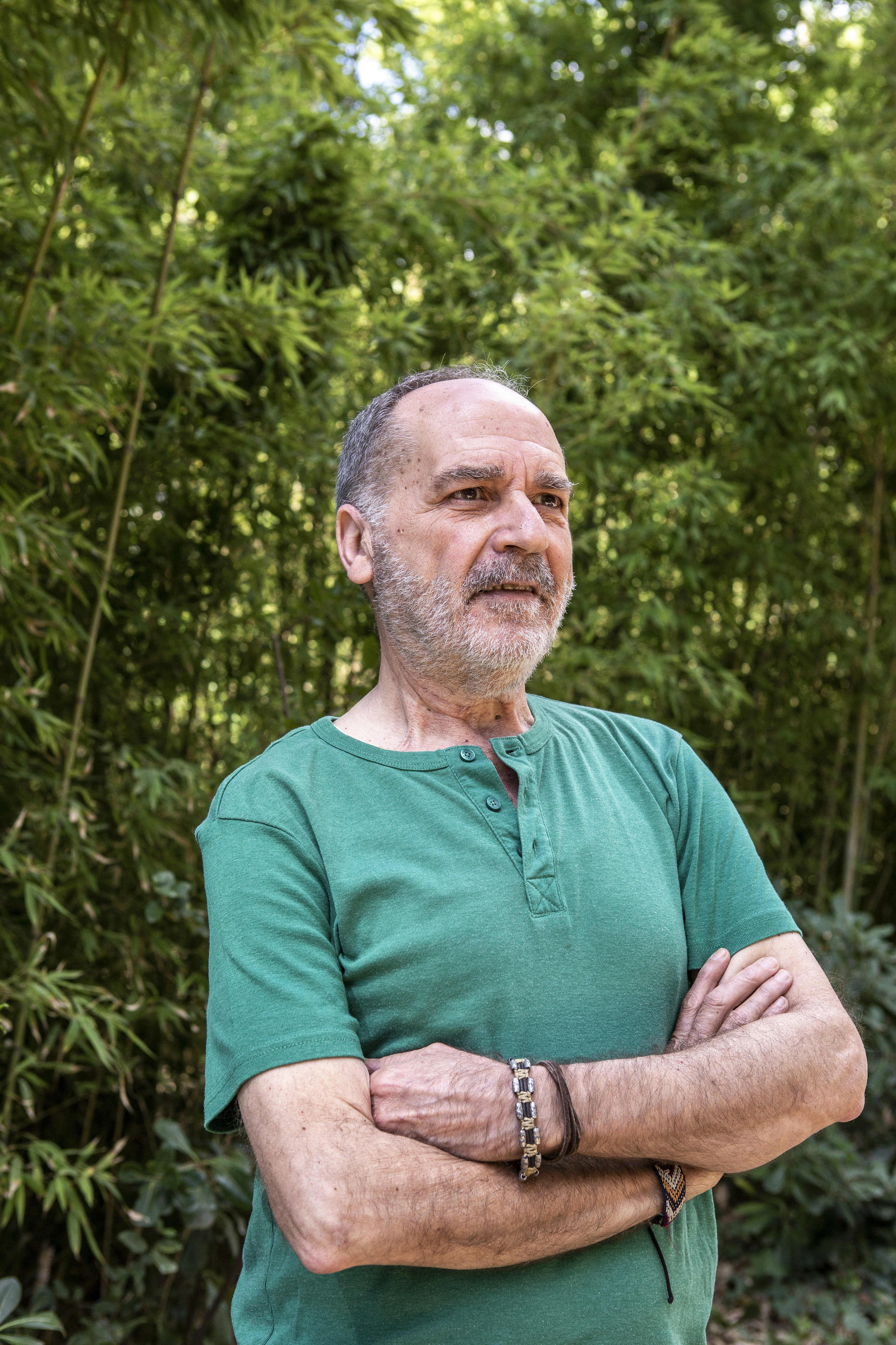 A man standing with his arms crossed in front of trees