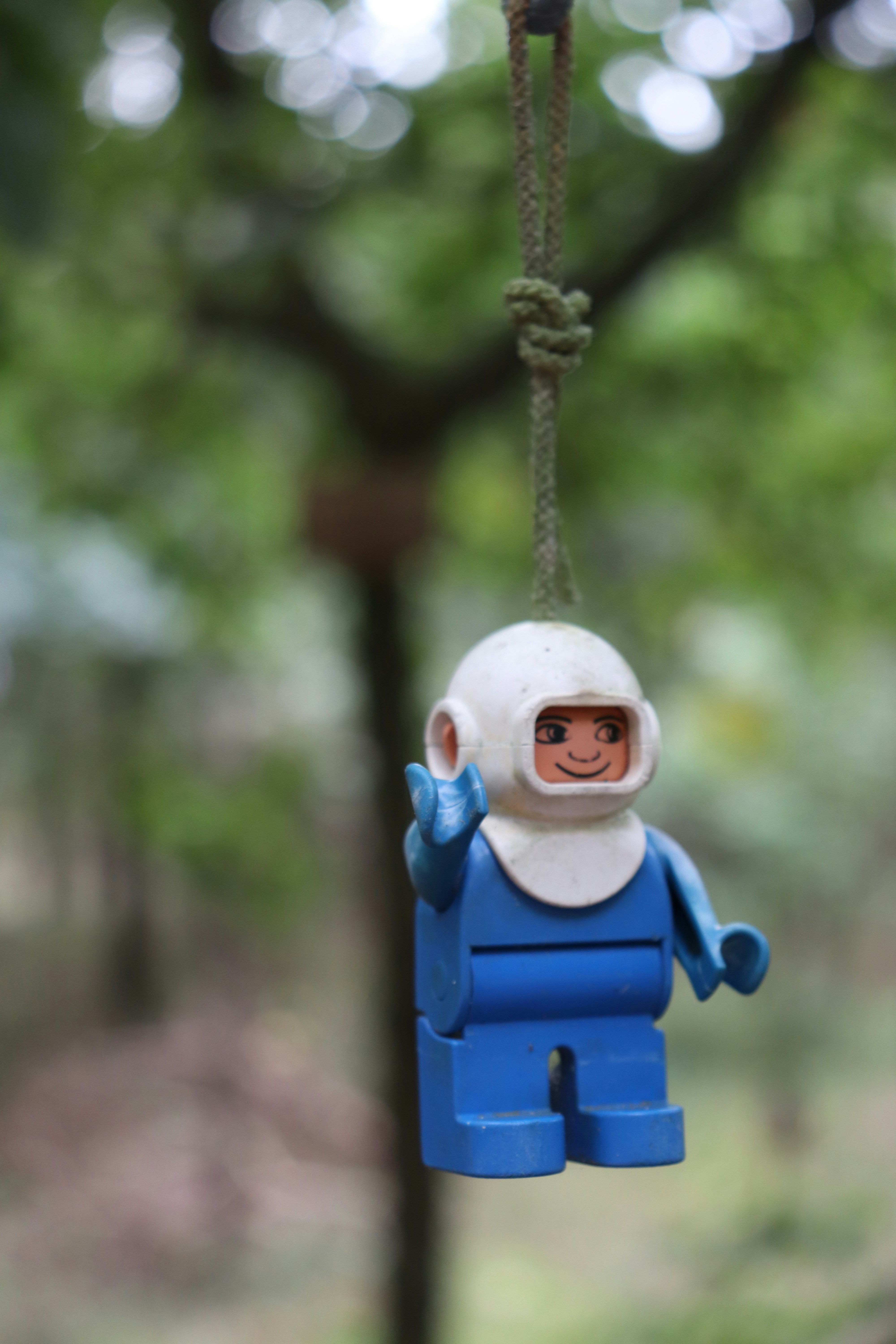 A lego man hanging from a rope in a forest