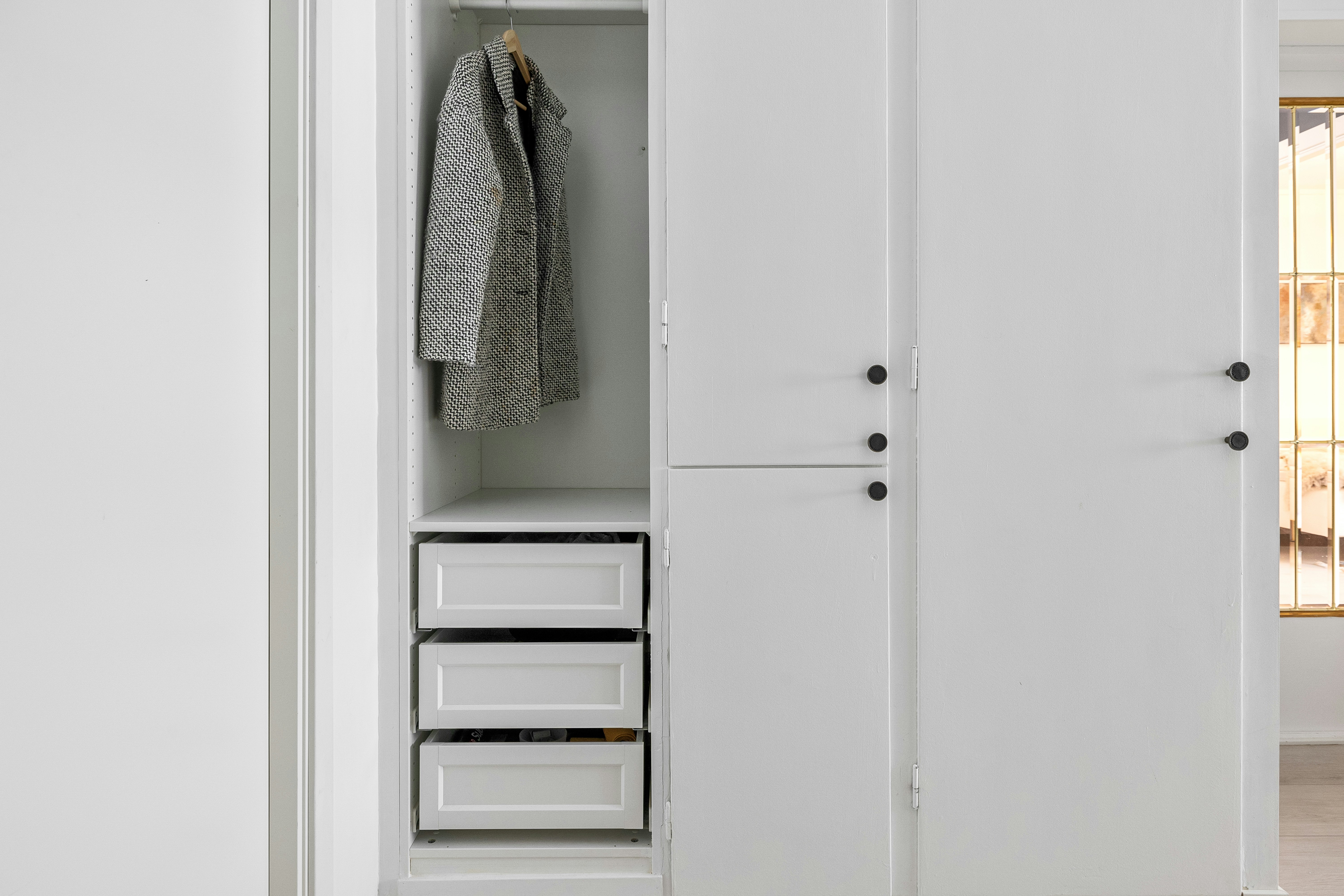 A white closet with drawers and a coat rack