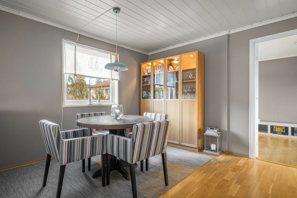 Gray dining room with large window, wooden floor, round table, and elegant bookshelf nearby