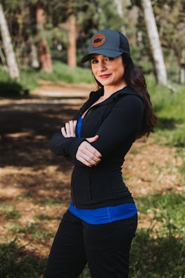 A woman standing in the woods wearing a baseball cap